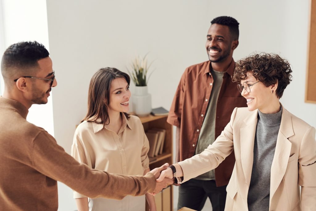 Four people in a business setting, two men and two women, smiling and shaking hands